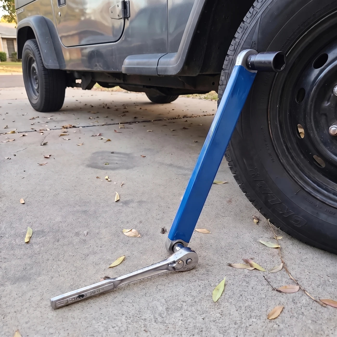 The bar leaning on a Jeep tire, a socket on one end and a ratchet on the other